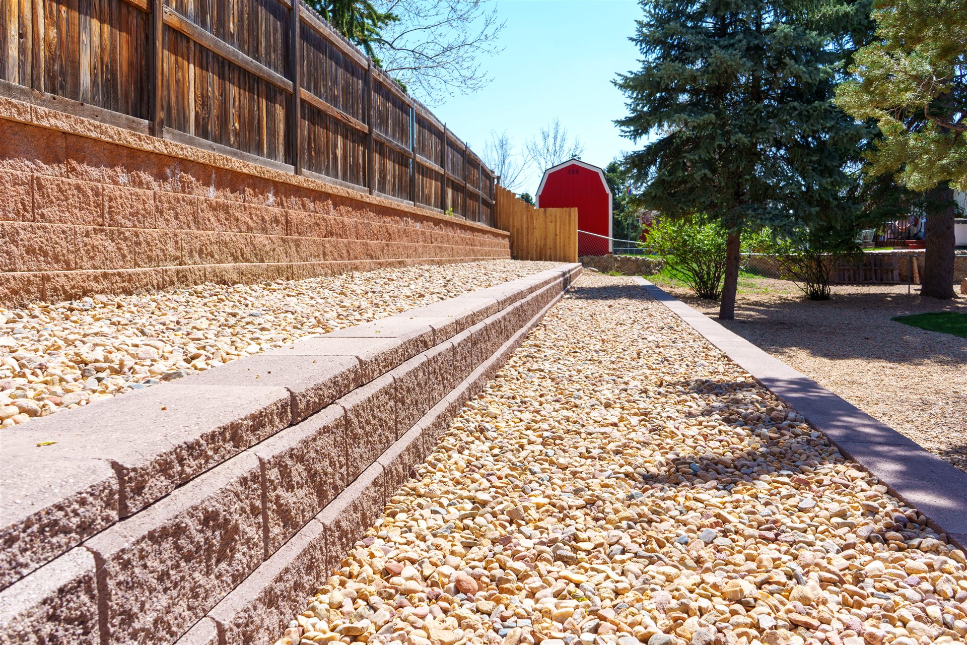 River rock path between block retaining walls along a fence