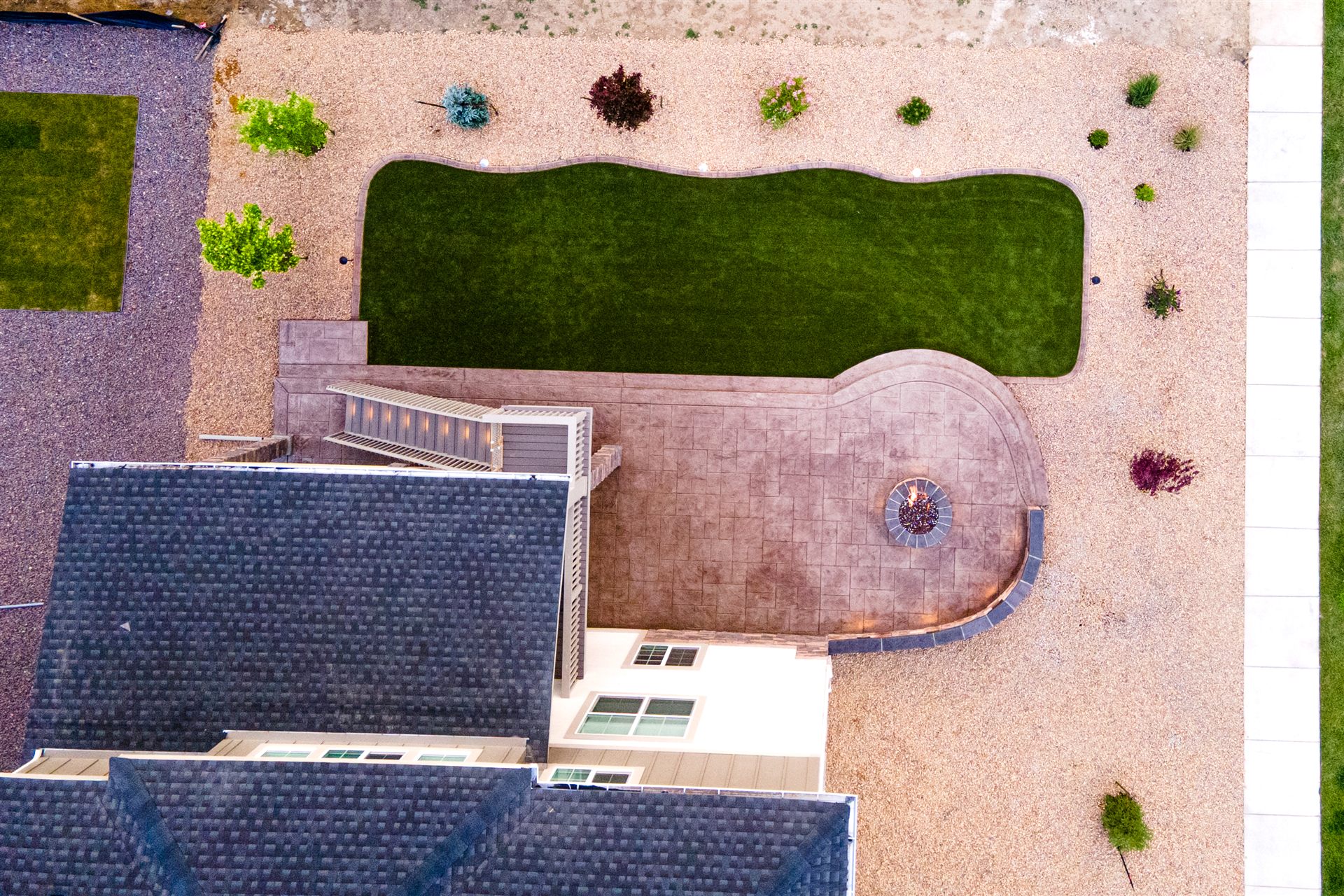Aerial view of a curved stamped concrete patio, fire pit and synthetic turf lawn in Brighton