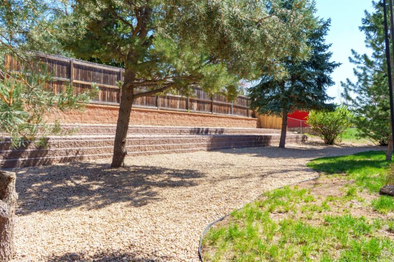 Two levels of block retaining walls behind pine trees in Brighton, CO