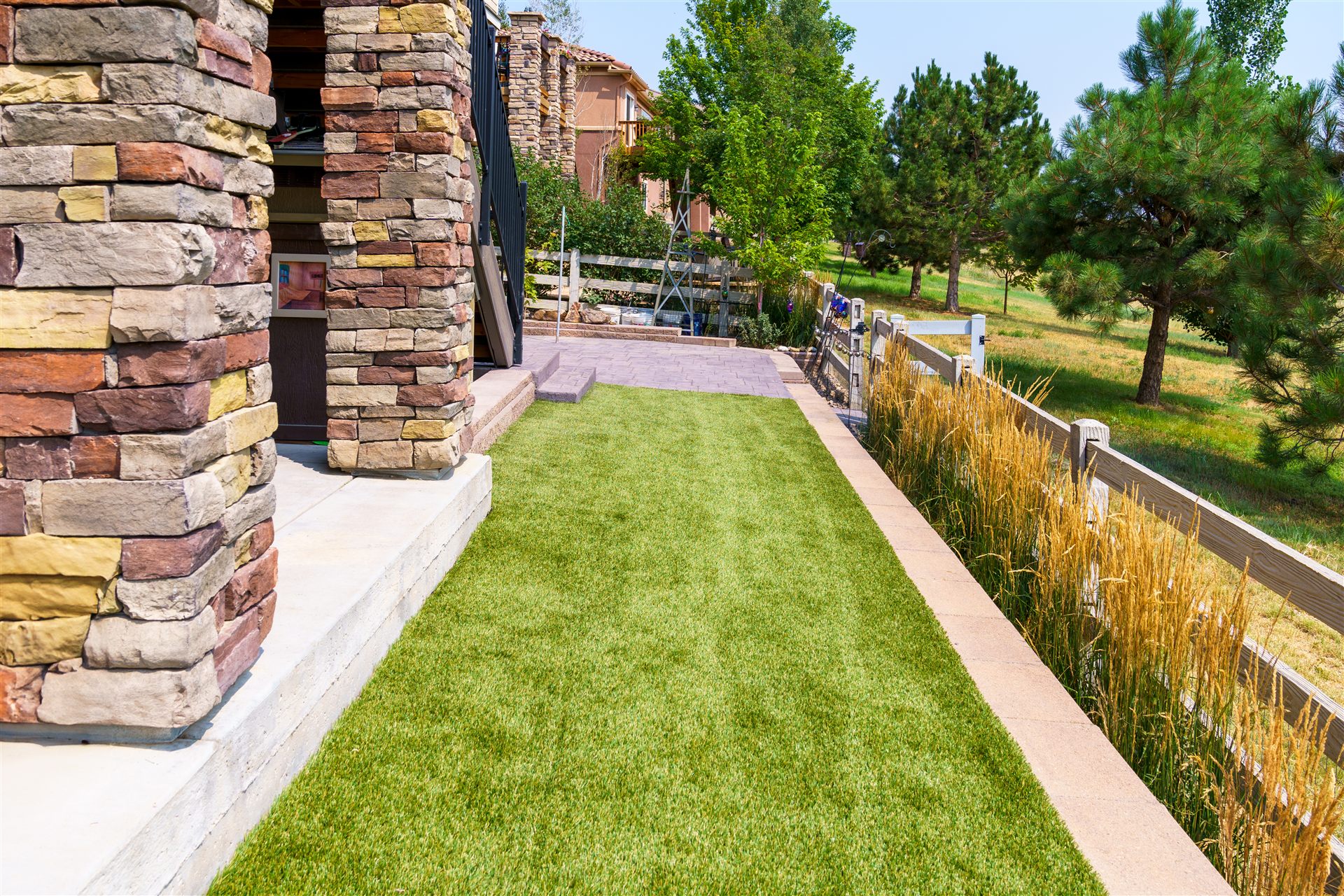 Synthetic turf side yard beside stone columns and a rail fence
