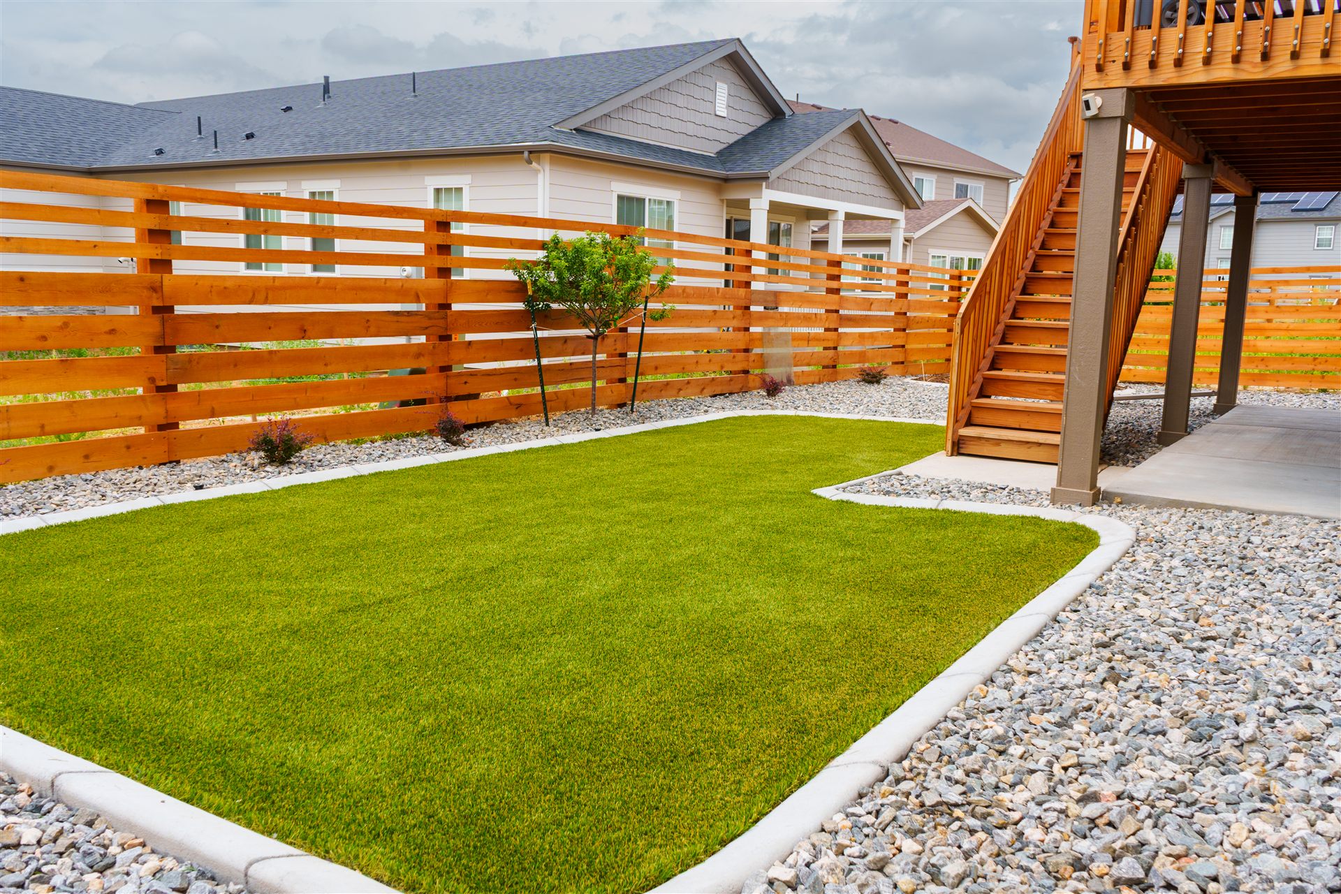 Curved sod lawn with a concrete edge and rock border under a deck