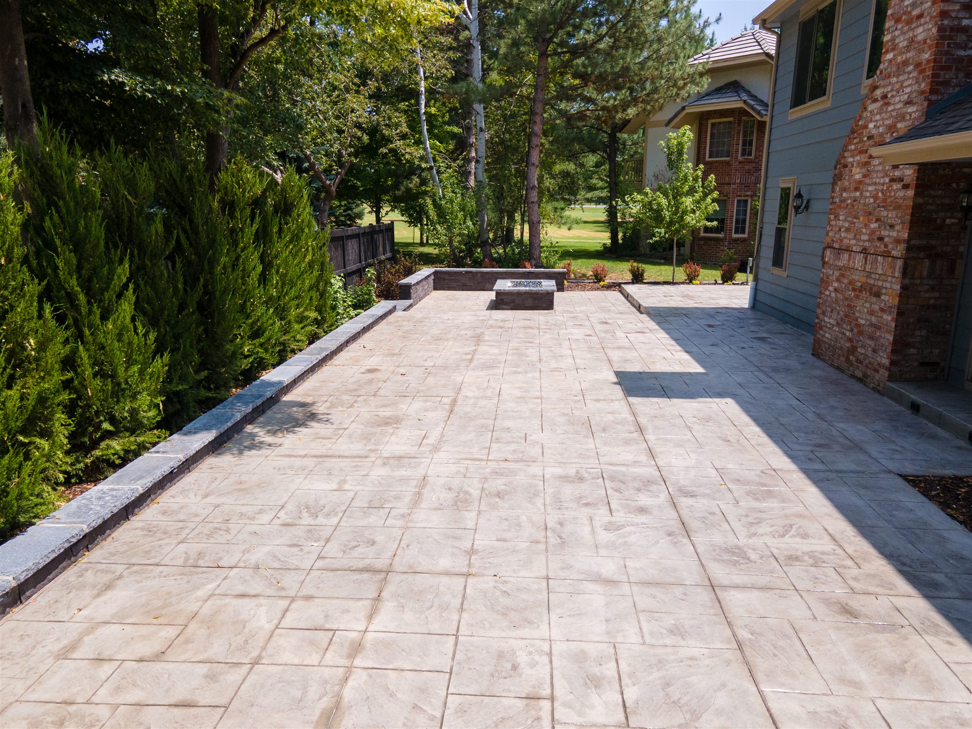 Long stamped concrete patio along a home under mature trees