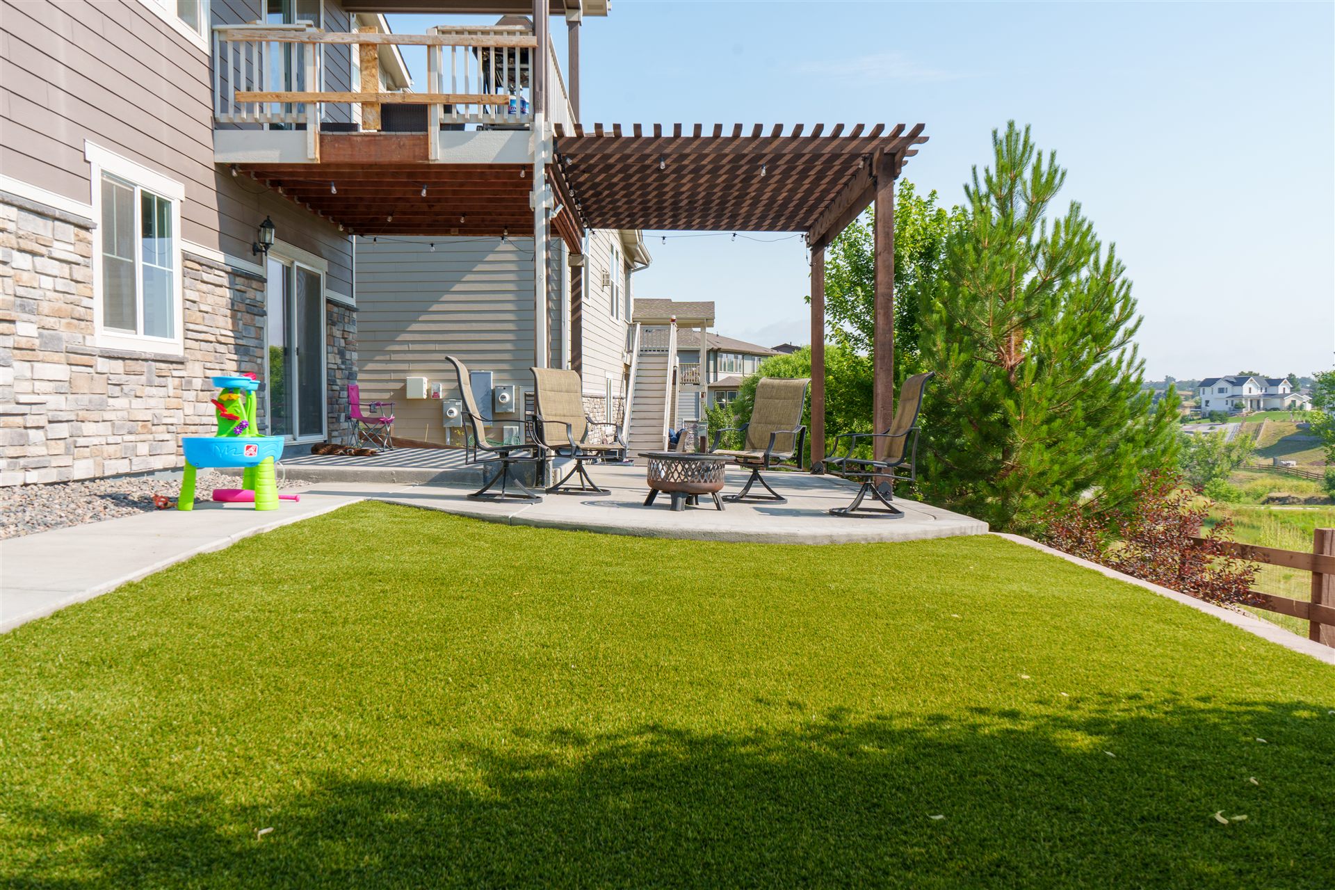 Wide view of a pergola patio and synthetic turf lawn below an upper deck