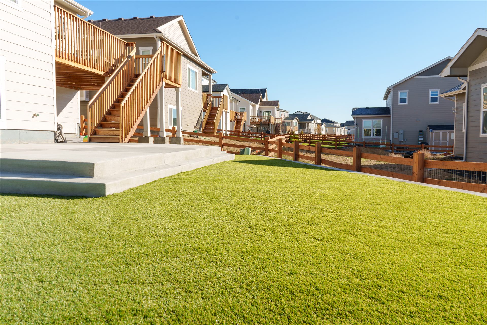 Synthetic turf backyard with concrete steps behind a new home