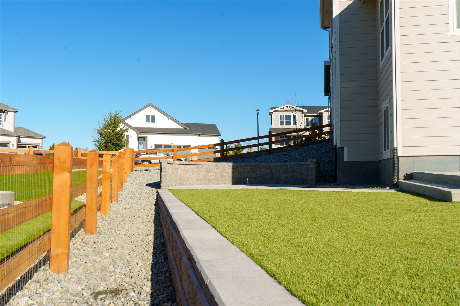 Capped block retaining wall beside synthetic turf and a side gate