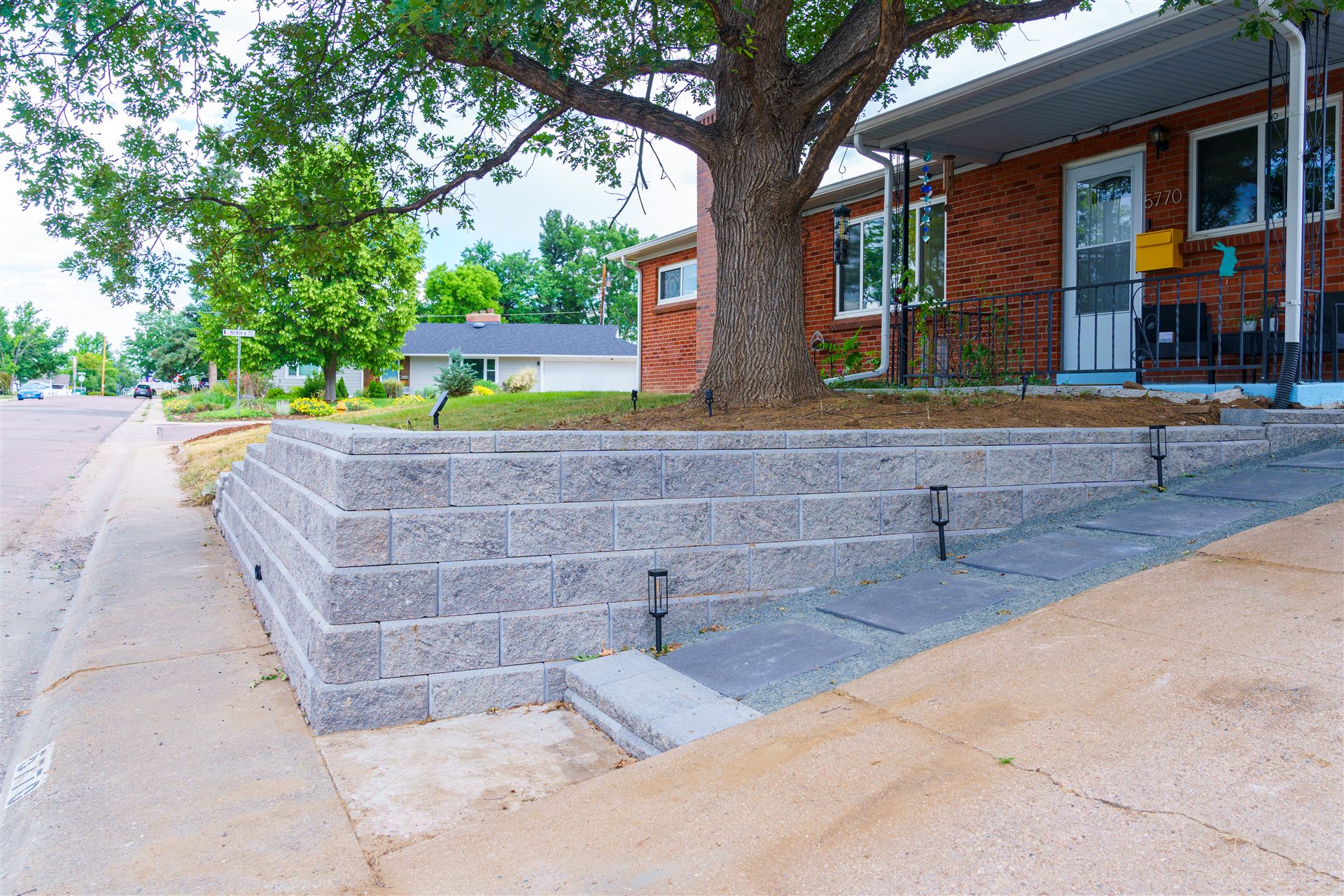Block retaining wall with lights along the sidewalk in front of a brick ranch