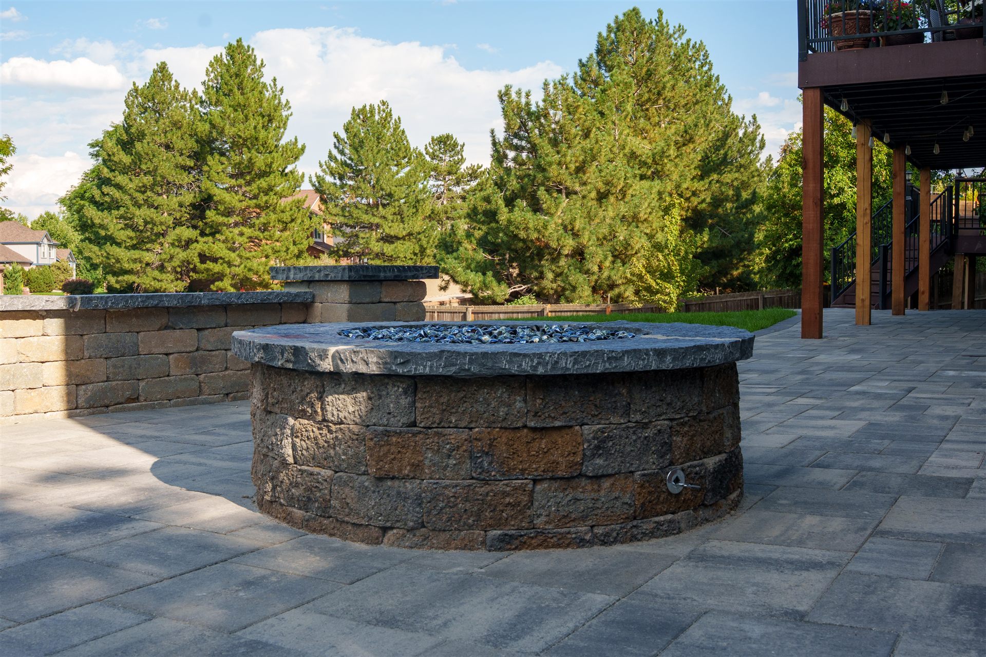 Round stone fire pit on a gray paver patio below a deck