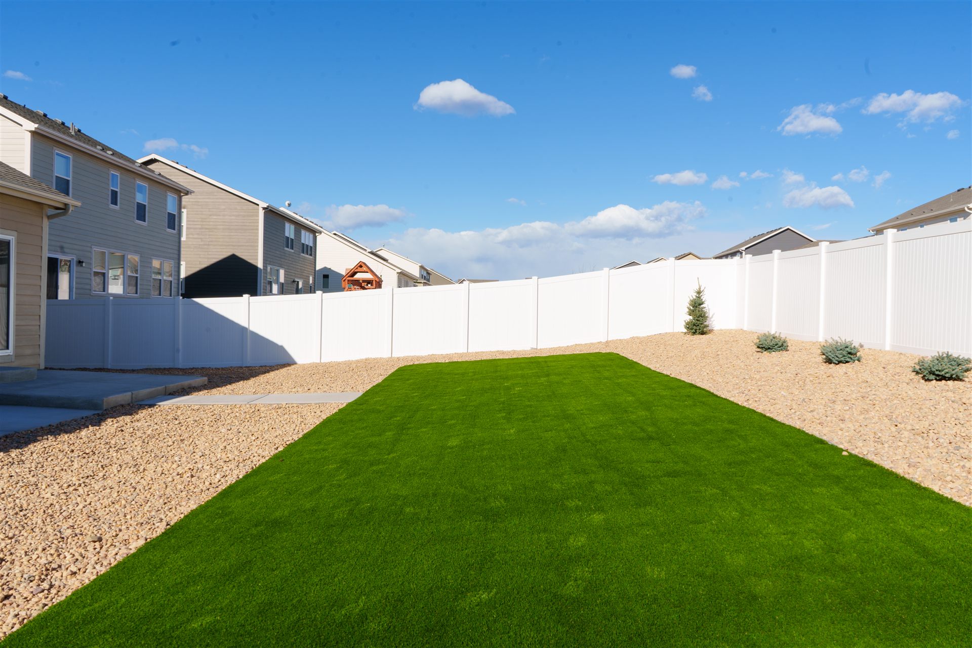 Synthetic turf lawn with rock landscaping behind a vinyl fence in Thornton