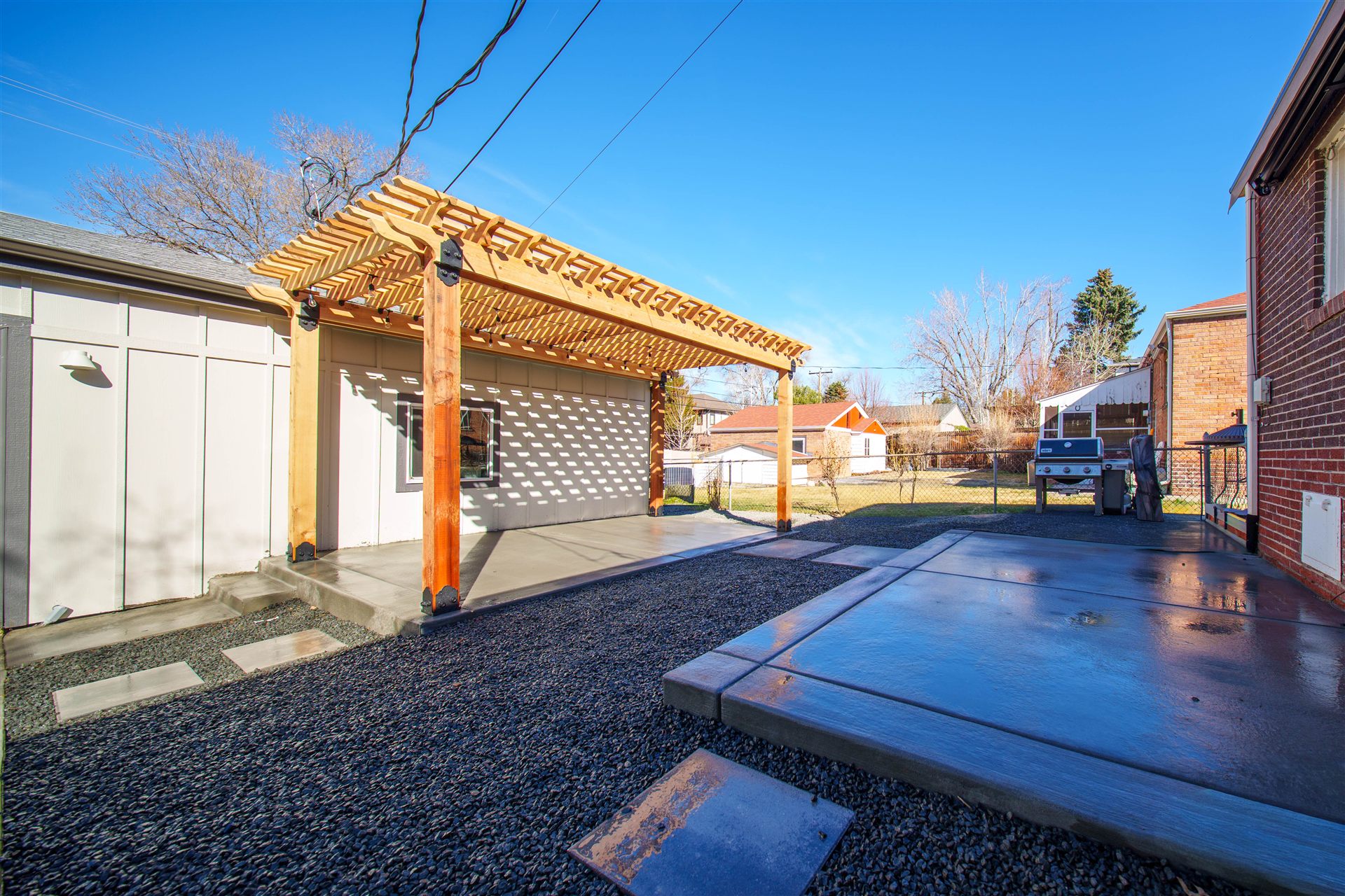 Pergola patio and a separate concrete grill pad next to a brick home