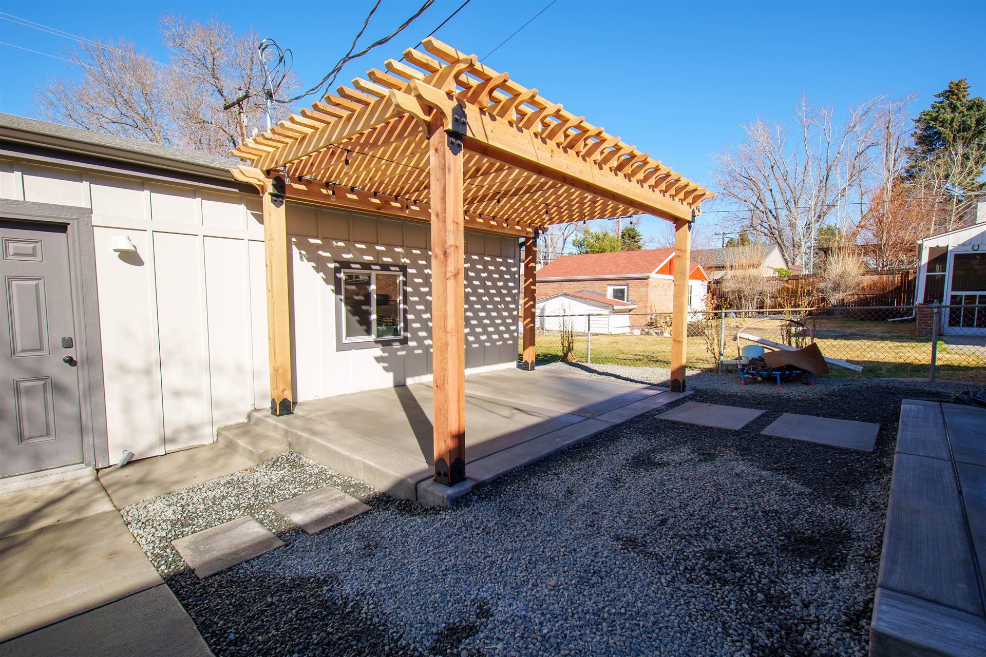 Freestanding wood pergola beside a garage with a gravel yard