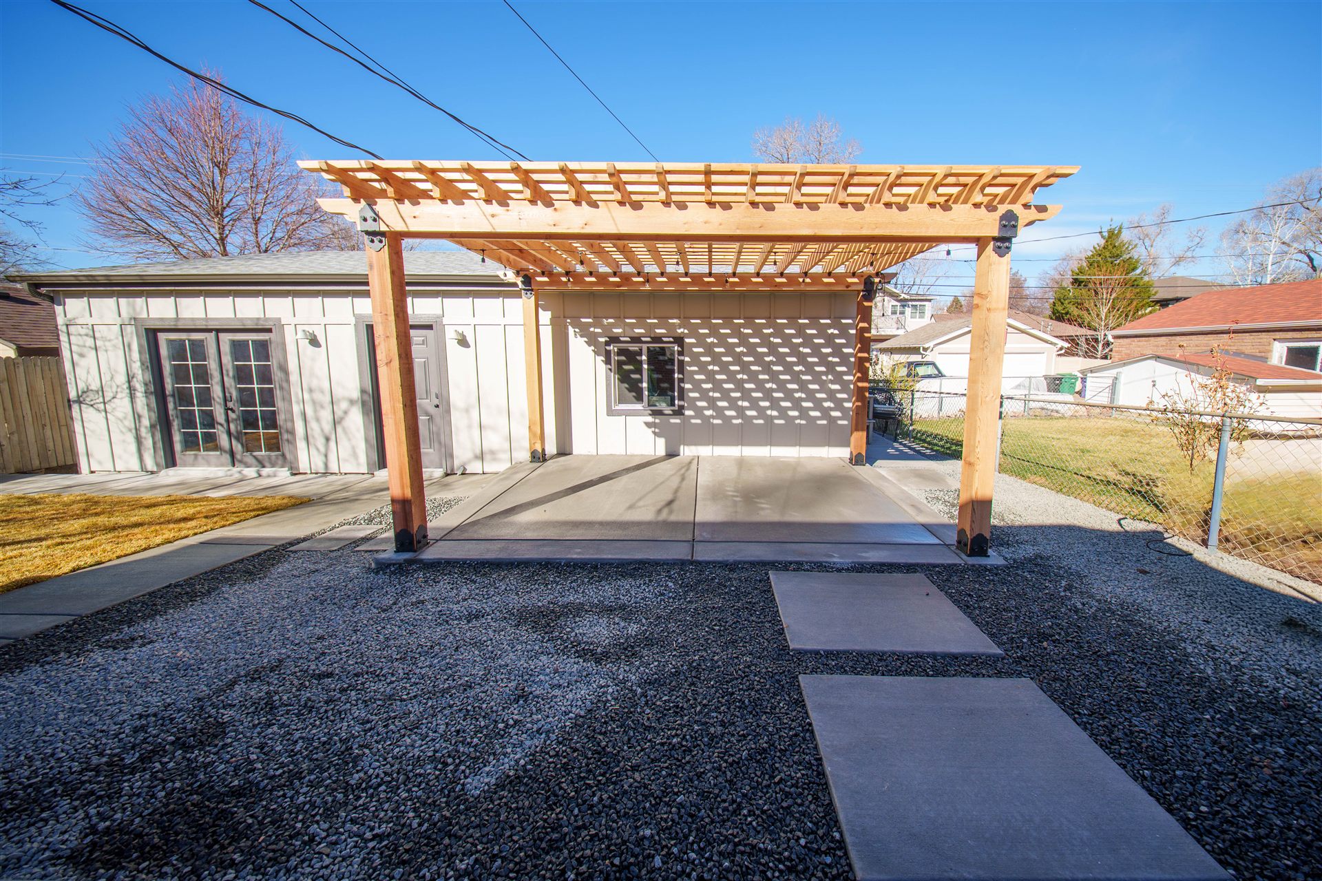 Wood pergola and concrete patio with stepping pads across a gravel yard