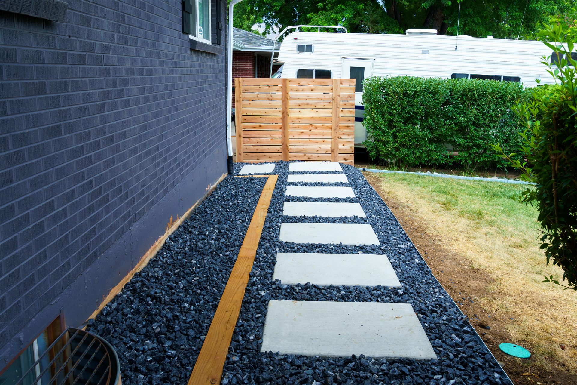 Side-yard concrete stepping pads in black rock leading to a wood gate
